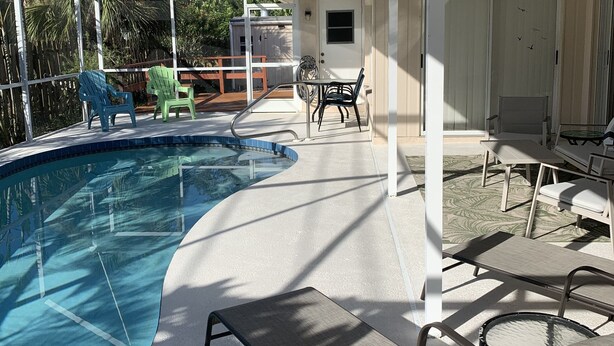 Ett utomhusområde med en pool som är delvis skyddad från väder och vind, utrustat med solstolar, ett bord och en takfläkt.