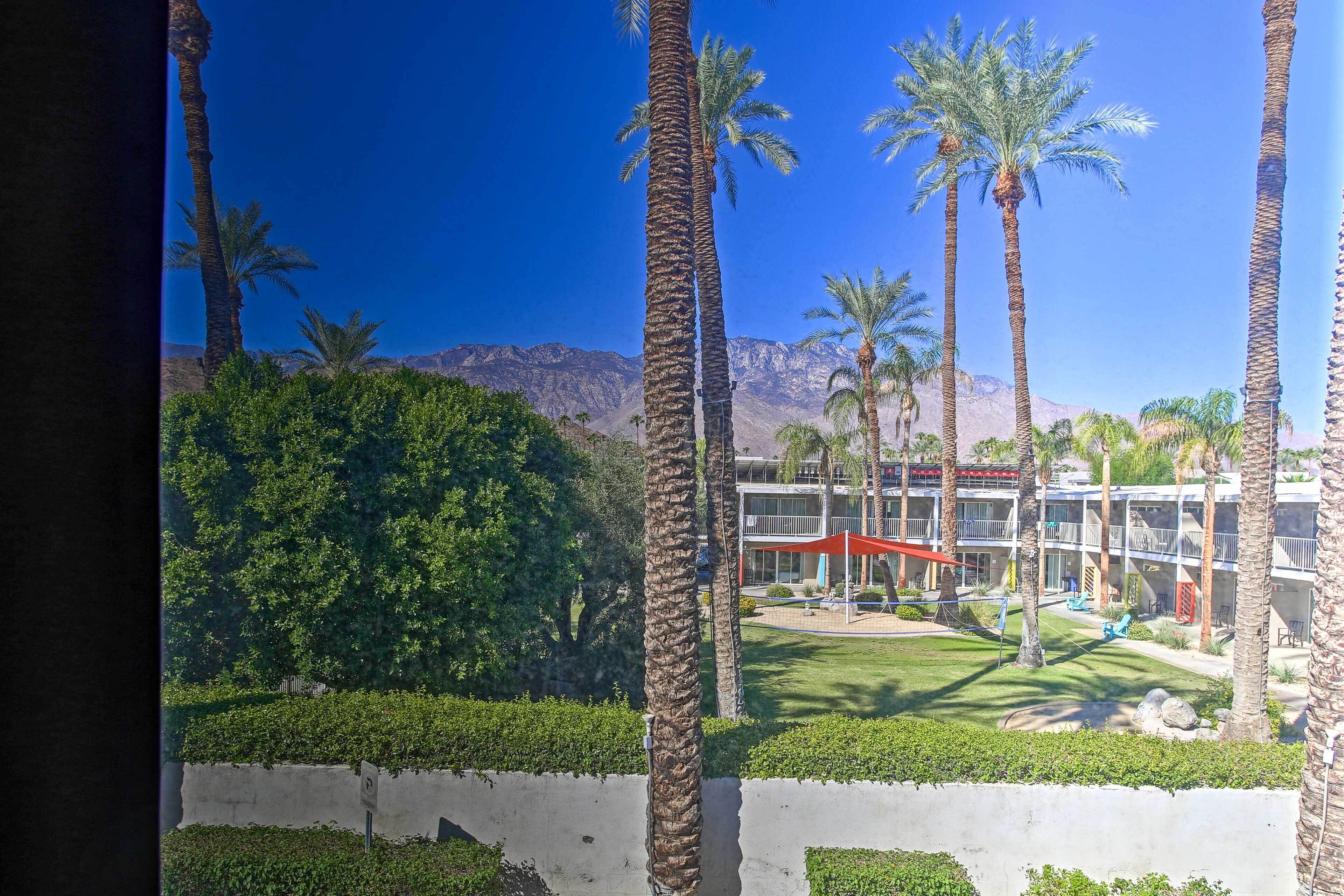 Un hotel con palmeras, un césped cuidado y el paisaje de una montaña al fondo.