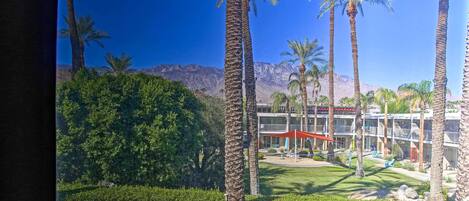Un hotel con palmeras, un césped cuidado y el paisaje de una montaña al fondo.