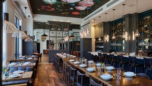 Un restaurant avec de longues tables en bois, des luminaires suspendus et un bar avec des étagères remplies de bouteilles.