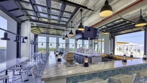 Un espace bar moderne doté de hauts plafonds, de grandes fenêtres et d’un long comptoir avec des tabourets.