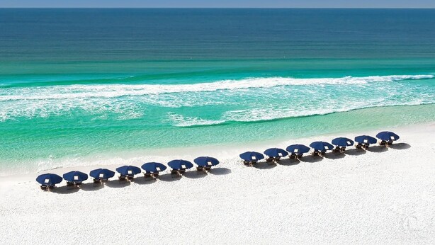 Une plage de sable blanc bordée d’une rangée de parasols bleus.