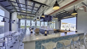 A modern bar area with high ceilings, large windows, and a long counter with bar stools. - BellaVida-Sandestin: Lakefront+Cart to Beach (Miramar Beach)