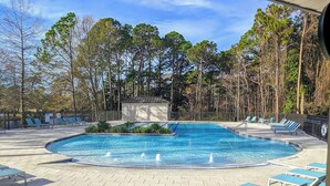 A swimming pool with lounge chairs and a small building, surrounded by trees.