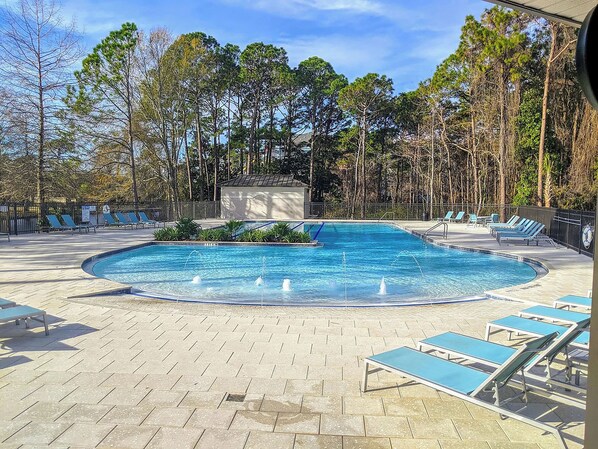 A swimming pool with lounge chairs and a small building, surrounded by trees.