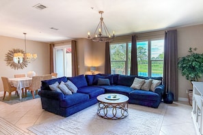 A living room with a sectional sofa, a round coffee table, and a dining area with a table and chairs.