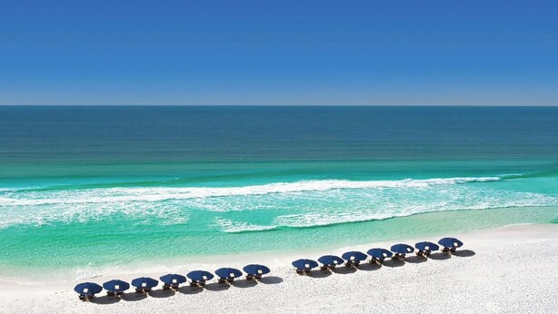 A beach with rows of blue umbrellas and white sand.