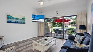 A living room with a sofa, coffee table, and TV. There's a sliding glass door leading to an outdoor area with a table and chairs. - CostaLuna-Beachwalk 2BR/2BA/Loft - Cart to Beach! (Miramar Beach)