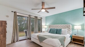 Ein Schlafzimmer mit einem großen Bett, einem Deckenventilator, einem Nachttisch und Blick ins Freie.