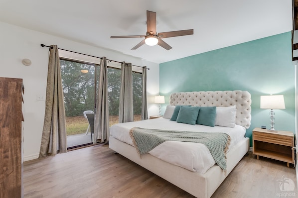 A bedroom with a large bed, a ceiling fan, a nightstand, and a view of the outdoors. - MermaidBay-Seagrove: Sleeps 8, Walk to Beach (Santa Rosa Beach)