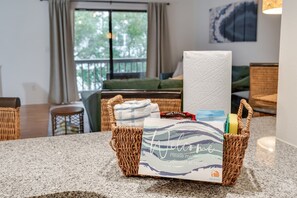 A wicker basket on a kitchen counter with a welcome card, a roll of paper towels, and a box of 100% Arabica coffee.
