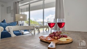 A dining table with a wooden board holding sliced meats, grapes, and cheese. Two glasses of red wine are on the table. - VillaIsla-3BR/2BA Villa - Steps from the Sand! (Santa Rosa Beach)