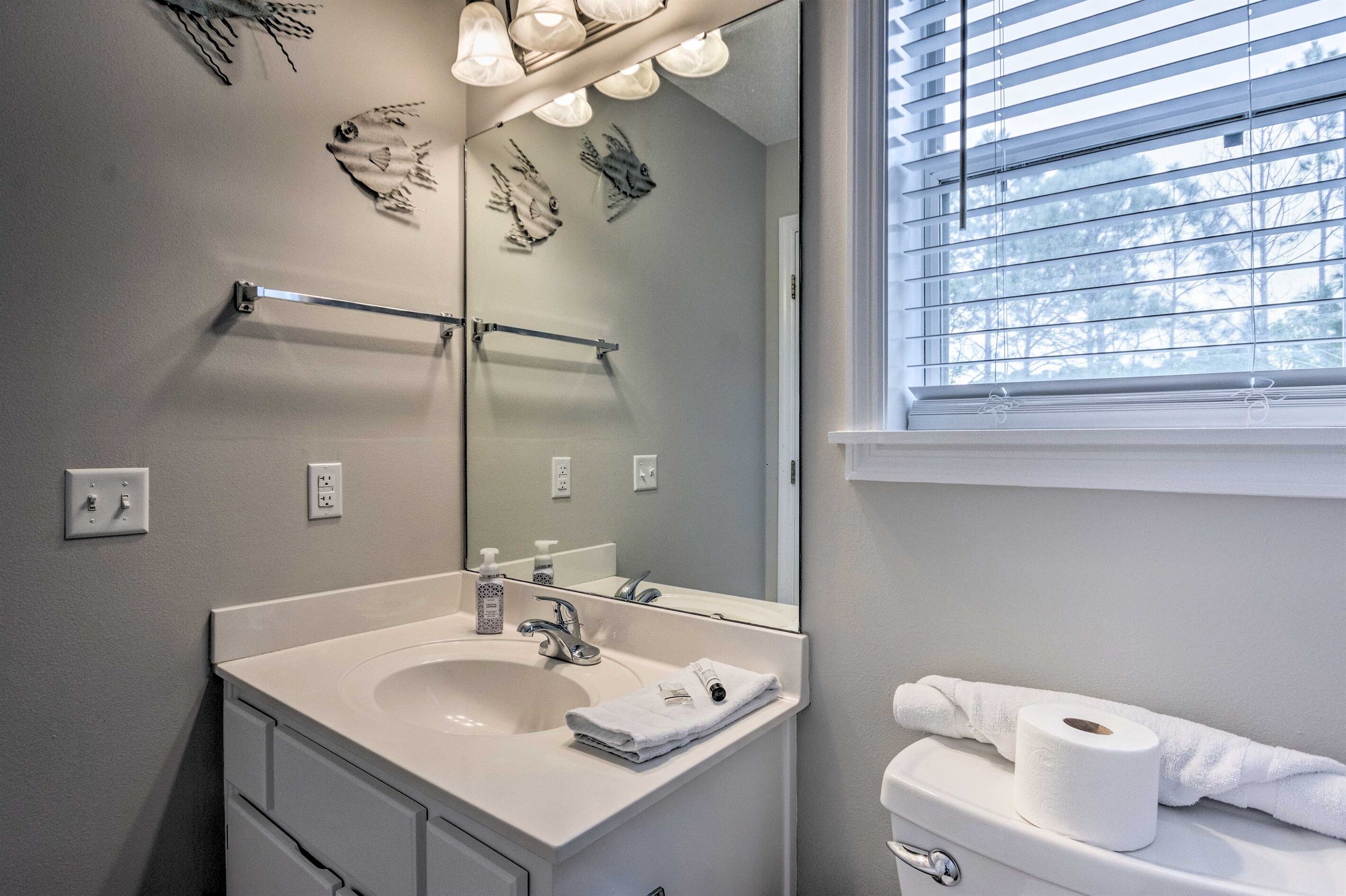 Une salle de bain équipée d’un lavabo, d’un miroir, d’un porte-serviettes, de toilettes et d’une fenêtre avec des stores.