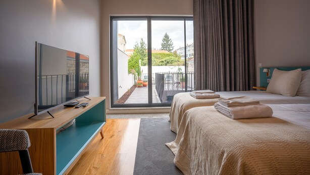 A modern hotel room with a large sliding glass door to the outside, a flat-screen TV, a wooden desk, and a bed with neatly folded towels. - Flores Studio - with terrace (Oporto)