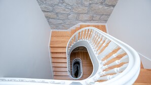 Un escalier en colimaçon avec des marches en bois et des balustrades blanches, menant à un mur de pierre.