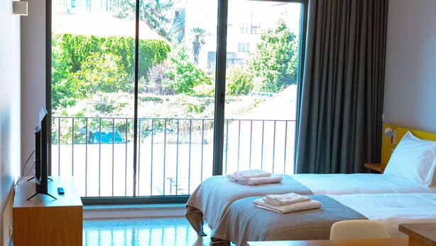 Une chambre d’hôtel équipée d’un lit, d’un bureau, d’une chaise et offrant une vue sur l’extérieur grâce à une grande fenêtre.
