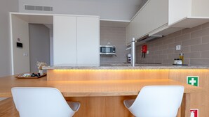 A modern kitchen with a wooden island, white chairs, a microwave, and a fire extinguisher. - Sá da Bandeira Studio - with balcony (Oporto)