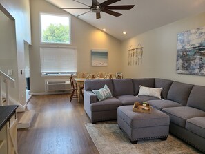 A modern living room with a sectional sofa, ottoman, and a dining area with a table and chairs.