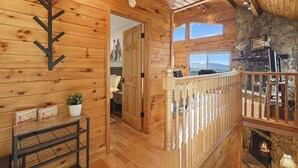 A wooden cabin interior with a stone fireplace, wooden walls, and a balcony overlooking a scenic view. - Amazing Views*HotTub*Sauna*GameRooms Dog-friendly! (Beech Mountain)
