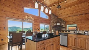 A spacious kitchen with wooden cabinets, a large island, and a stone fireplace. - Amazing Views*HotTub*Sauna*GameRooms Dog-friendly! (Beech Mountain)