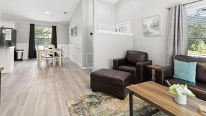 A modern living room with a brown leather sofa, a wooden coffee table, and a dining area with a white table and chairs.