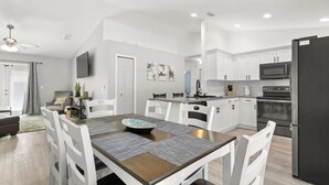 A modern kitchen with white cabinets, a black refrigerator, and a dining area with a wooden table and white chairs.