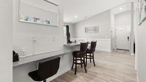 A modern kitchen with a white countertop, two bar stools, and a large mirror.