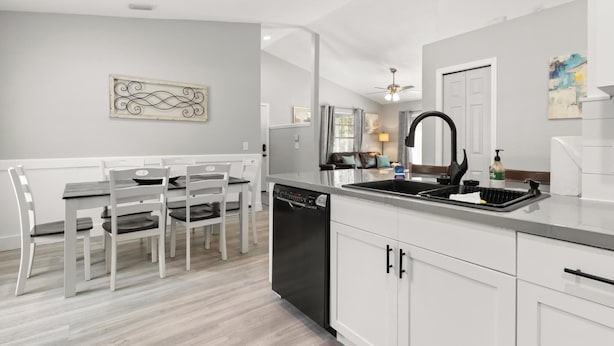 A modern kitchen with white cabinetry, a black dishwasher, and a grey countertop.