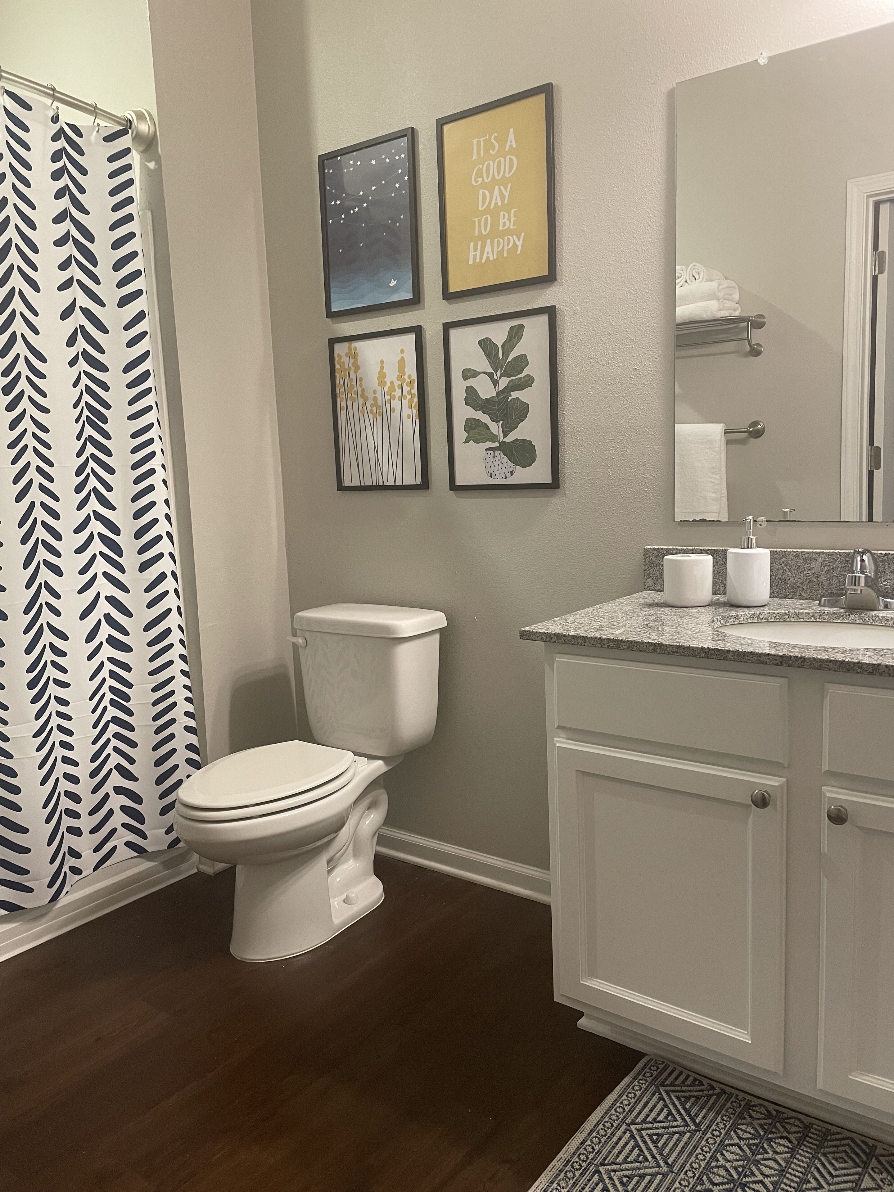 Une salle de bain avec des toilettes, un lavabo et un rideau de douche. Des tableaux encadrés ornent le mur.