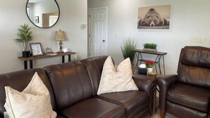 Un salon avec un canapé en cuir marron, un miroir rond, un certificat encadré, une lampe et un tableau accroché au mur.