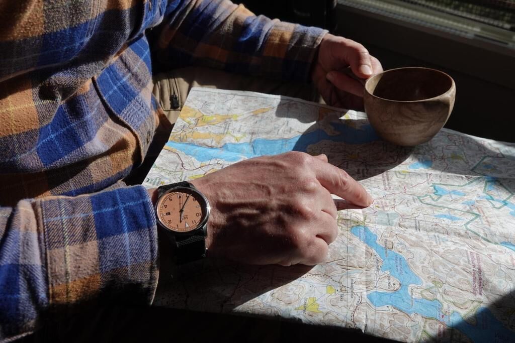 A person holding a map and a cup, with a watch on their wrist.