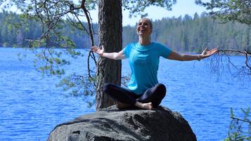 Une personne assise sur un rocher au bord d’un lac, avec des arbres en arrière-plan.