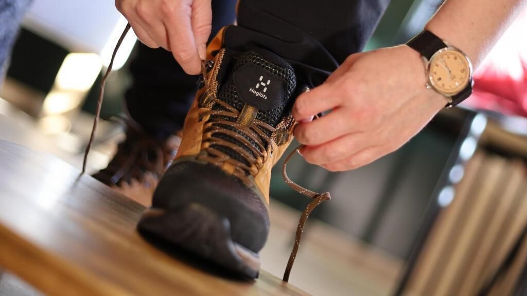 Una persona atándose los cordones de un zapato con un logotipo de marca visible.