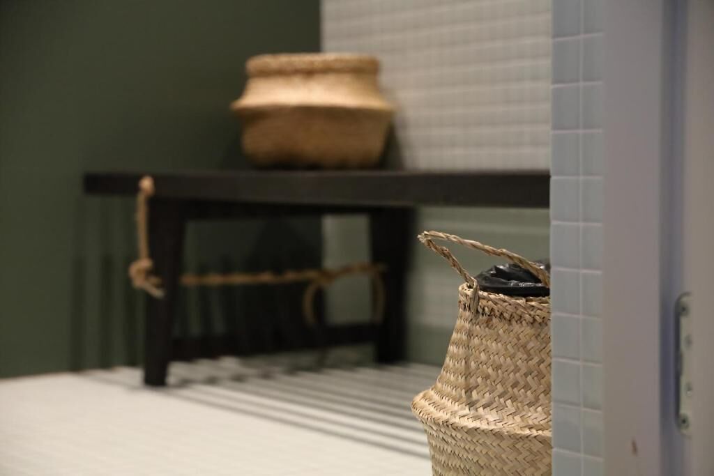 A bathroom with a woven basket on the floor, a small woven stool, and a woven basket on a shelf.