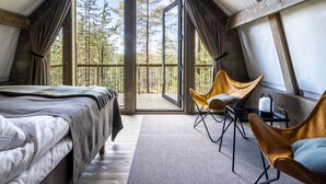 Una habitación cálida tipo cabaña con una cama, dos sillones y un ventanal con vistas al bosque.