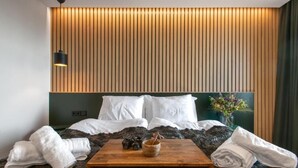 Una habitación de hotel moderna con una cama grande, un cabecero de madera, una mesita de madera y un aplique de pared.