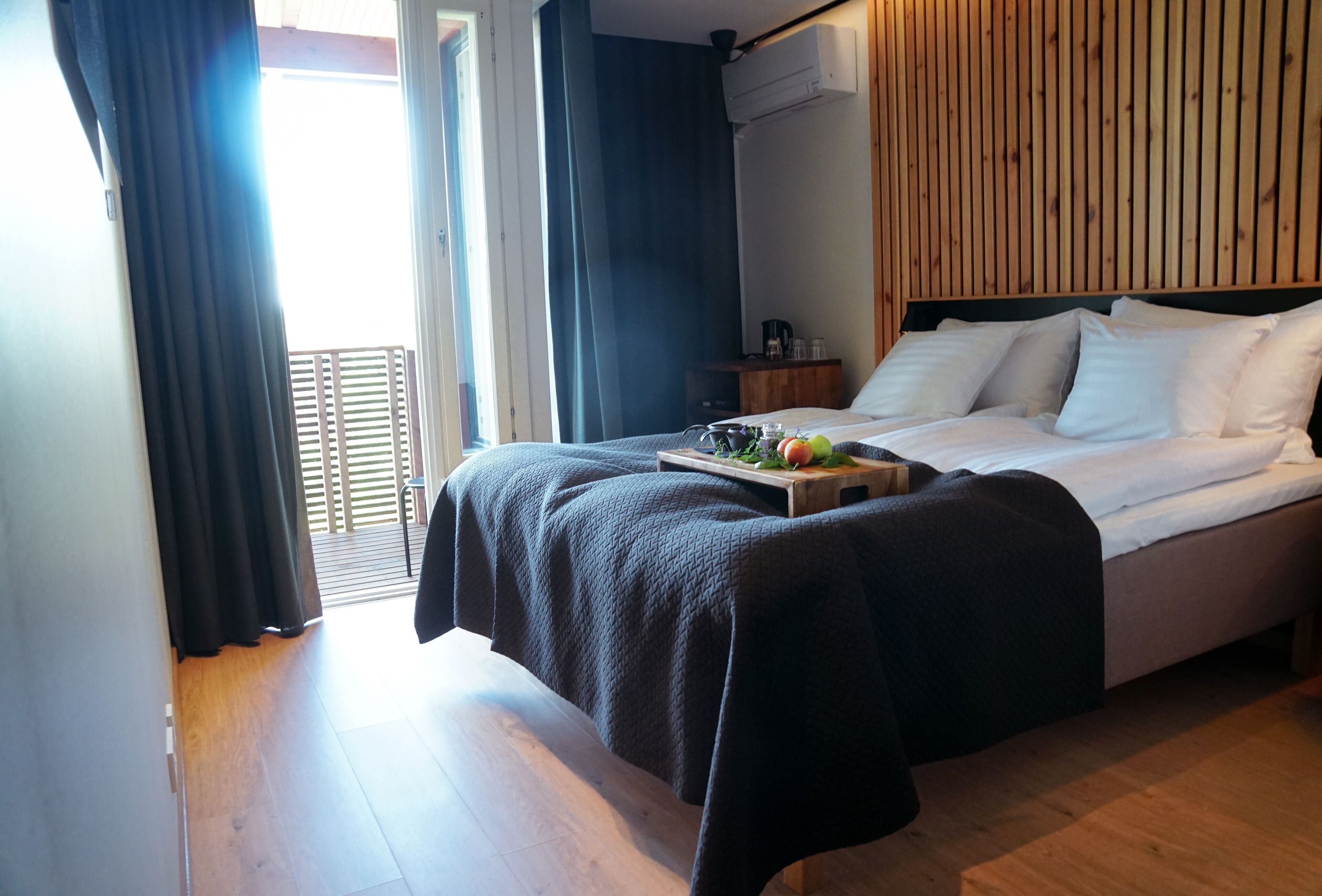 Una camera d'hotel con un letto, una testiera in legno, un comodino con una lampada e una finestra con tende.