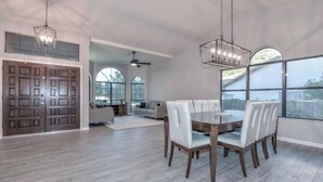 Un'ampia sala da pranzo con un tavolo e sedie in legno, ampie finestre e una ventola a soffitto.