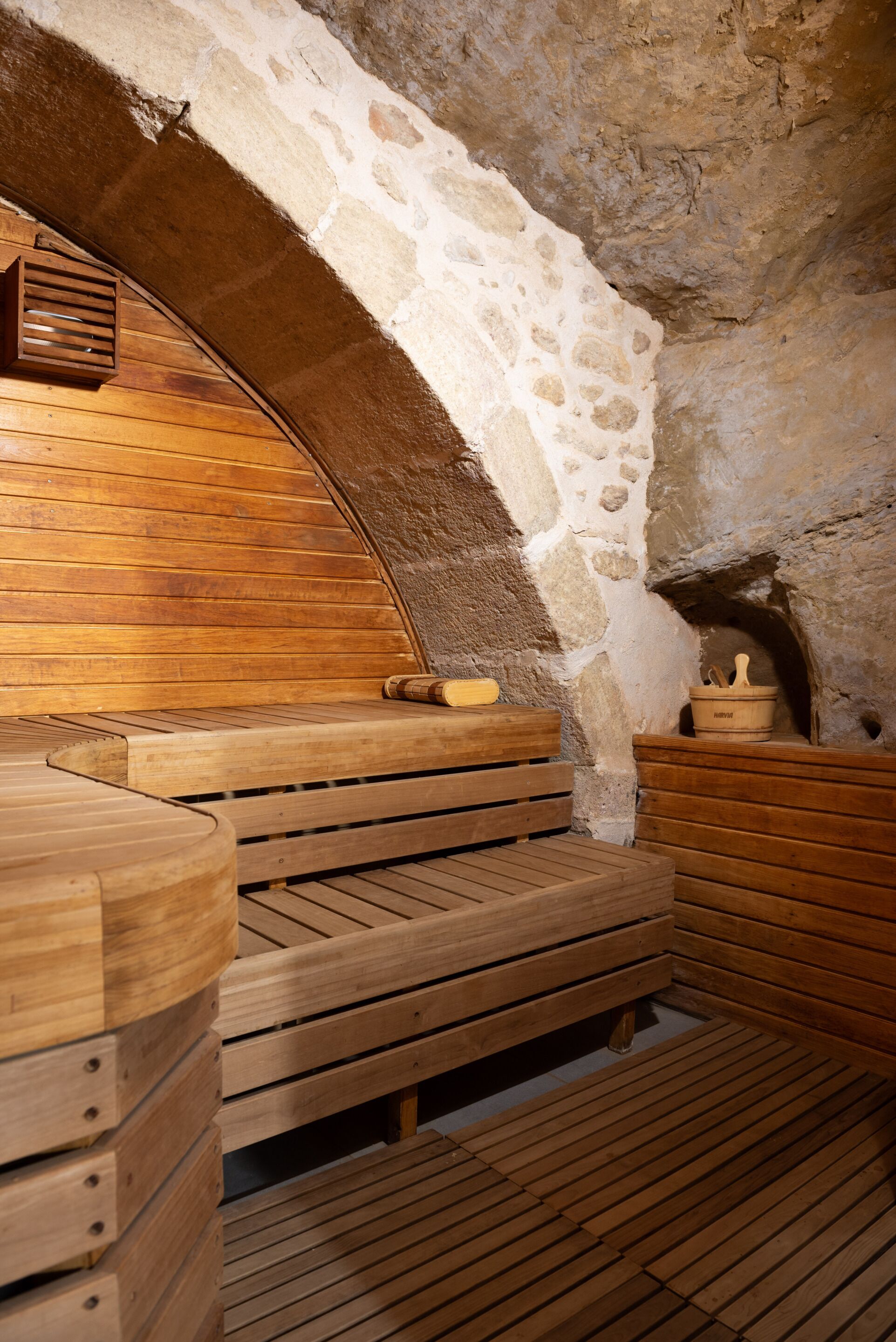 Una sauna de paredes de piedra con bancos de madera y un banco de madera con un perchero para toallas.