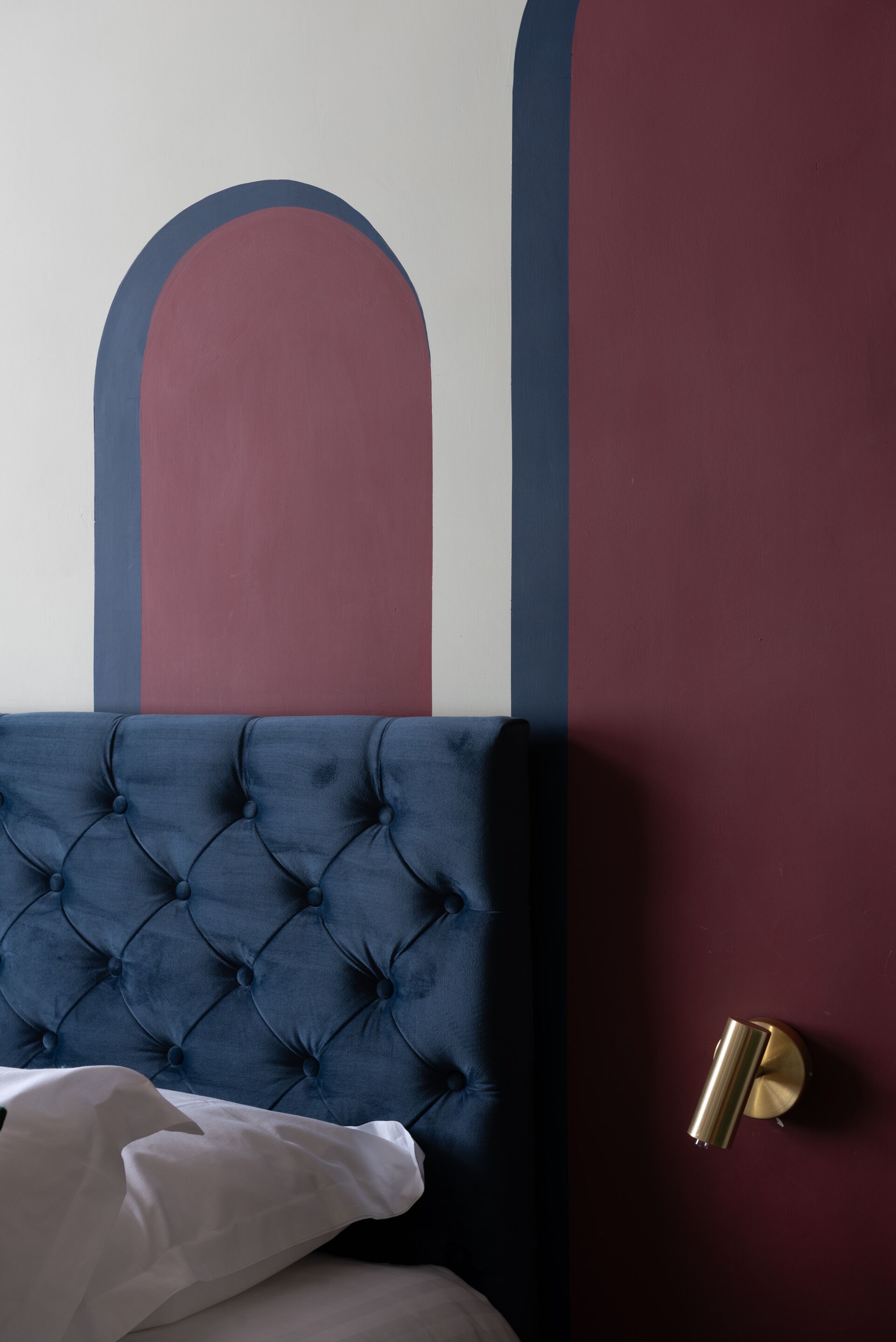 A bed with a tufted headboard, a wall with geometric patterns, and a wall-mounted light fixture.
