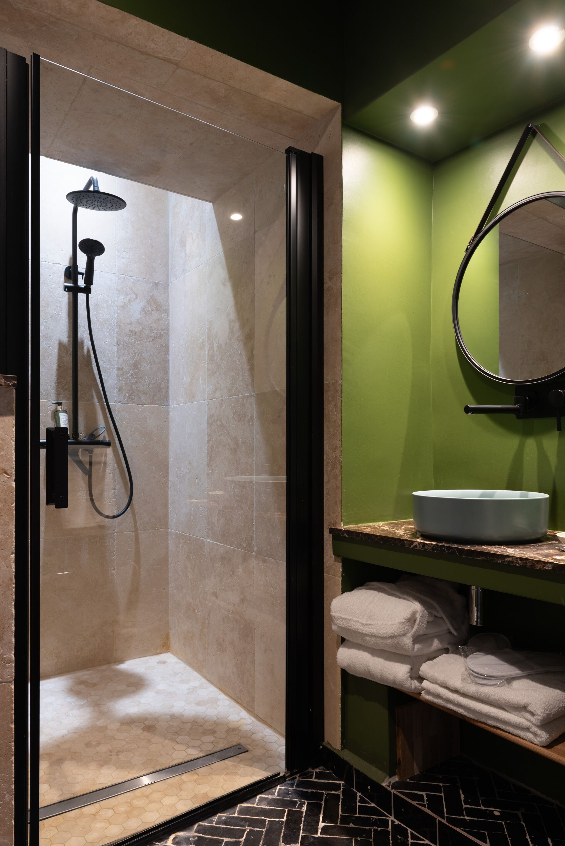A modern bathroom with a glass-enclosed shower, a round mirror, and a sink with a marble countertop.