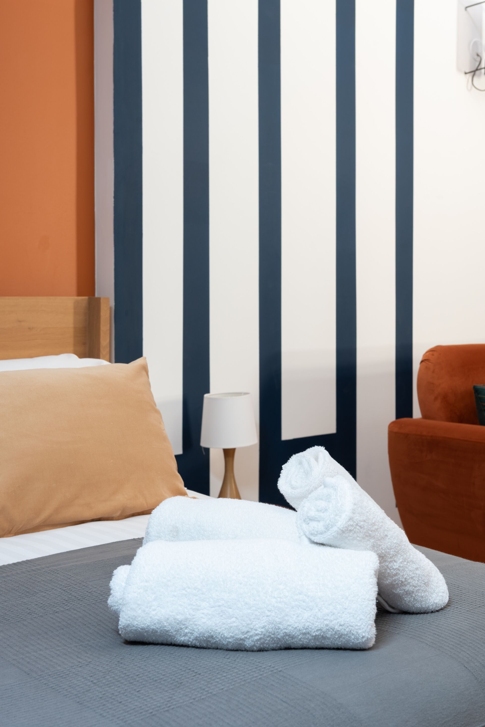 A neatly made bed with a brown pillow, two white towels, and a wooden headboard.