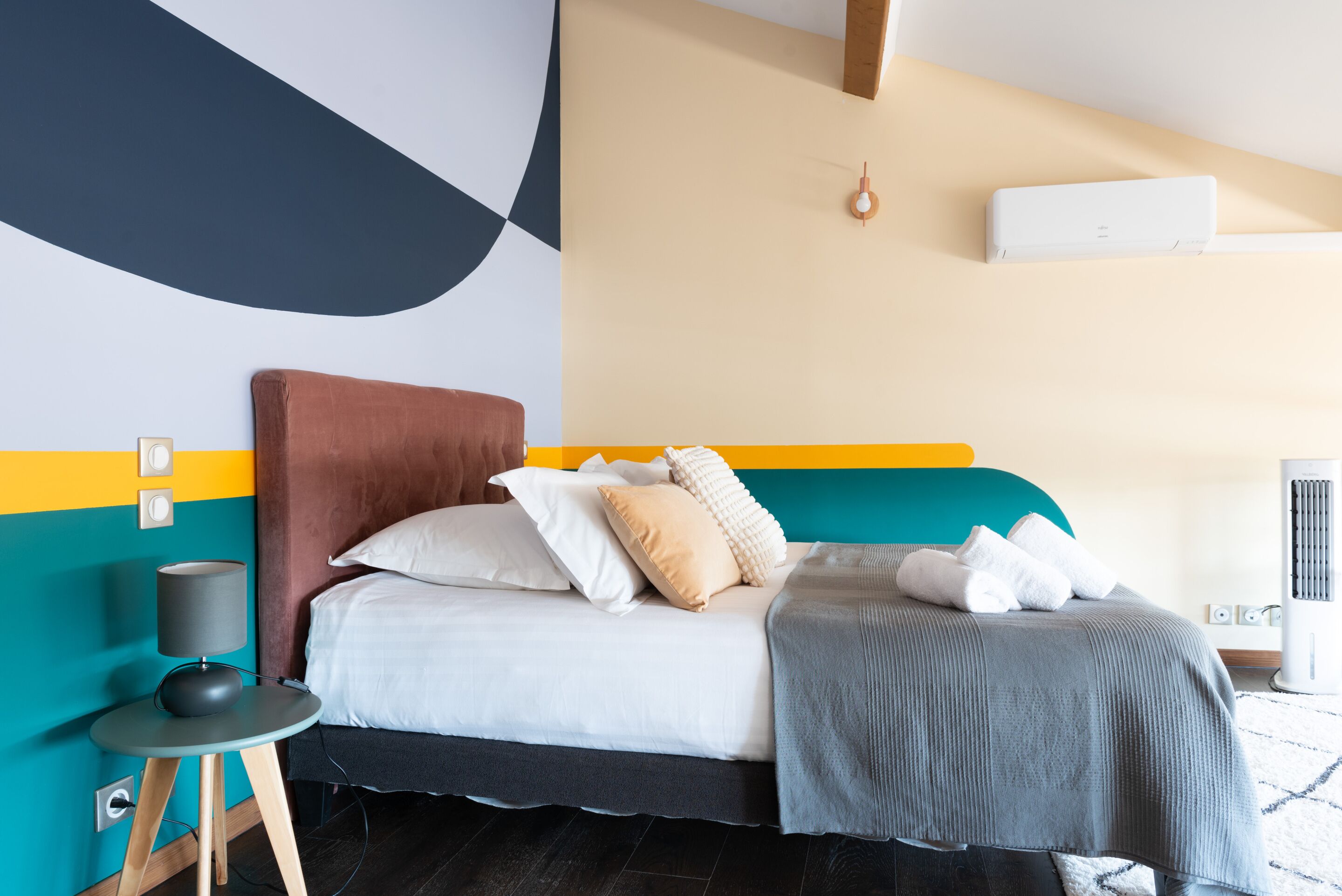 Une chambre moderne avec un lit, une table de chevet et un climatiseur fixé au mur.