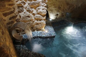 Un área de hidromasaje con paredes de piedra, suelo de baldosas y una fuente de agua.