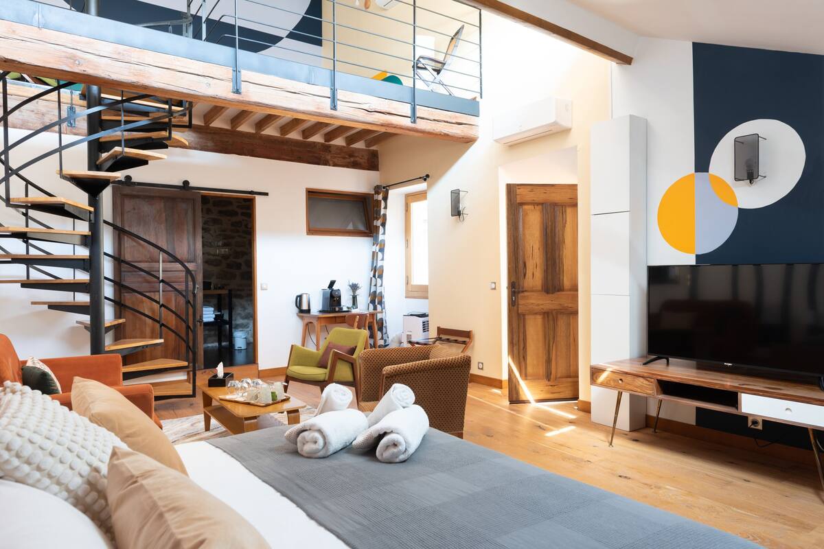 A spacious living area with a spiral staircase, a flat-screen TV, and a dining area.