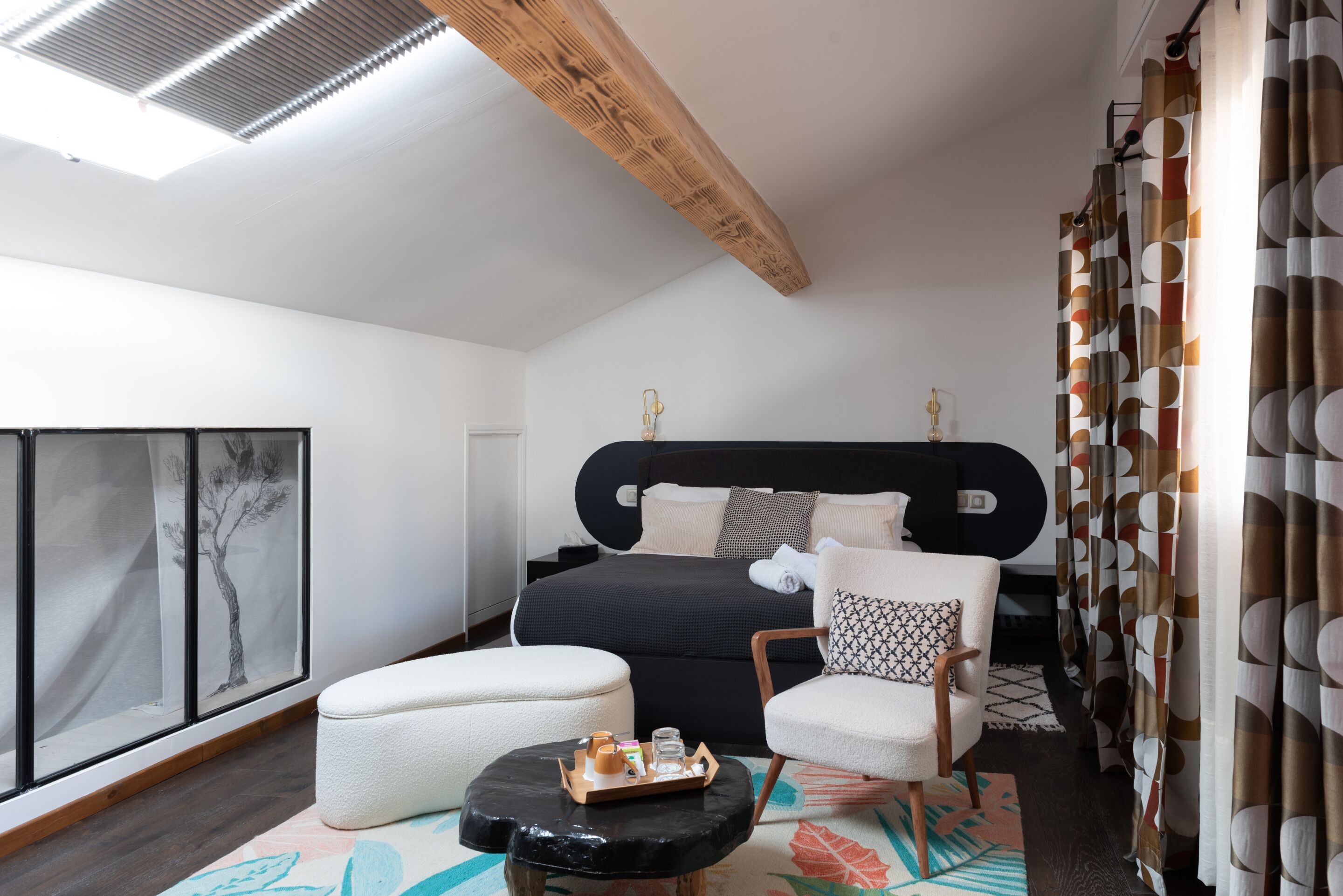 A modern bedroom with a large bed, a sitting area with a small table, and a large window with a view of trees.