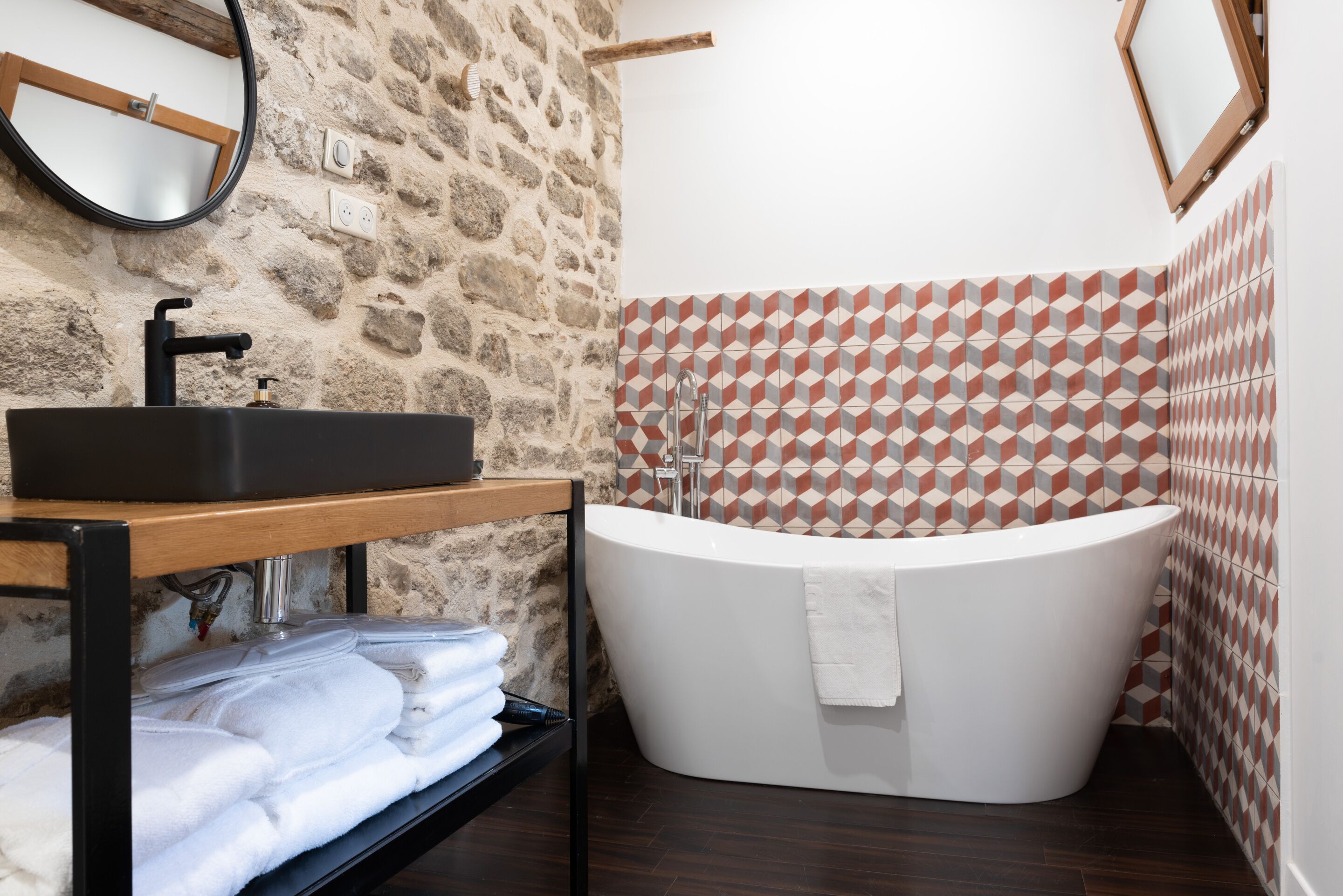 Une salle de bain moderne avec une baignoire sur pieds, un meuble-lavabo en bois doté d’un évier noir et un mur en pierre.