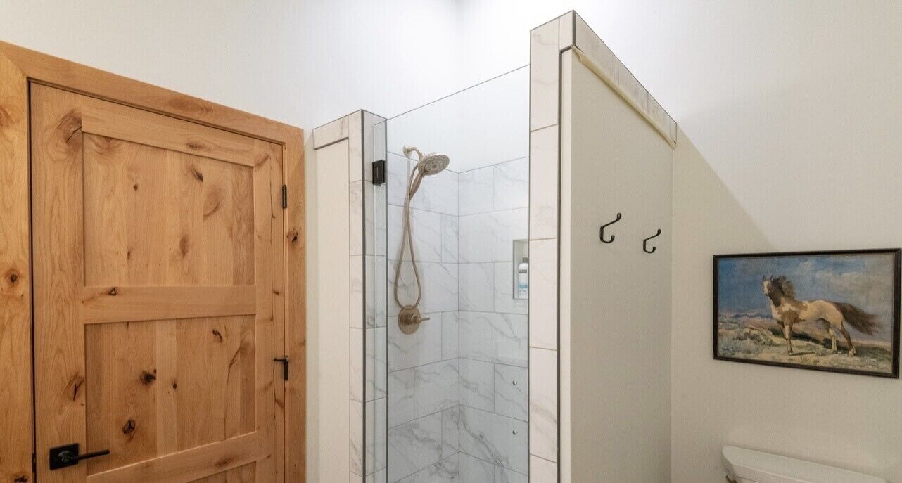 A bathroom with a wooden door, a glass shower enclosure, and a painting of a horse on the wall.