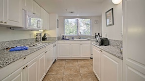 A kitchen with white cabinets, granite countertops, a microwave, a toaster, and a sink.
