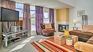 A modern living room with a flat-screen TV, a glass coffee table, a sofa, and a fireplace.